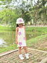 Young girl in a starfish-themed dress standing in a park by a pond.