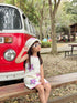 Young girl in a starfish dress sitting on a wooden bench with a red and white van in the background.