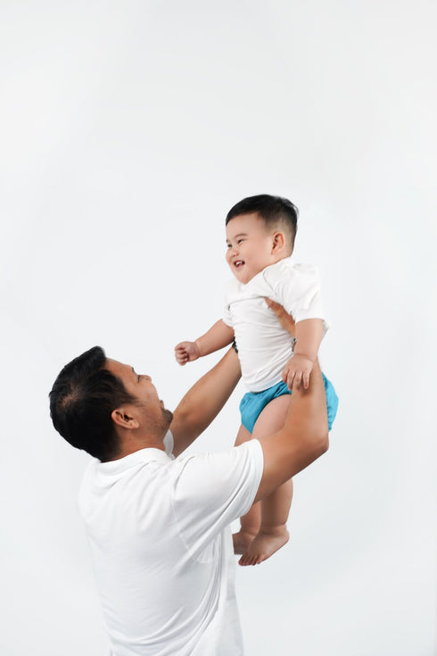 Dad lifting a happy baby wearing a blue reusable pants cloth nappy, Bali Bubs