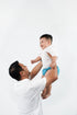 Dad lifting a happy baby wearing a blue reusable pants cloth nappy, Bali Bubs