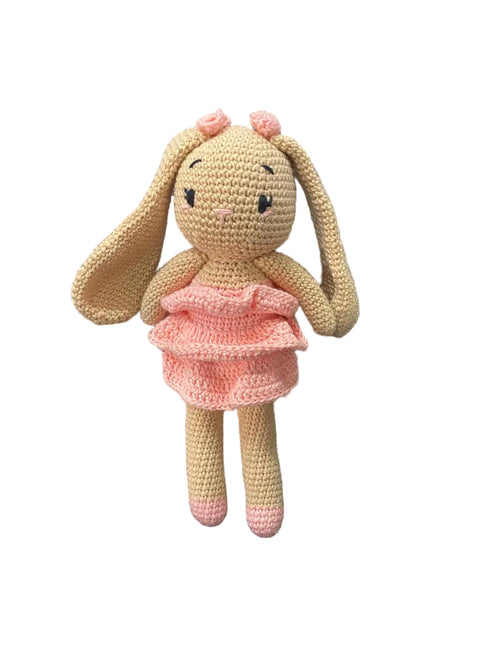 Crocheted bunny toy in a pink outfit sitting on a white background