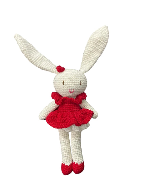 Crocheted bunny toy in a red dress sitting on a white background