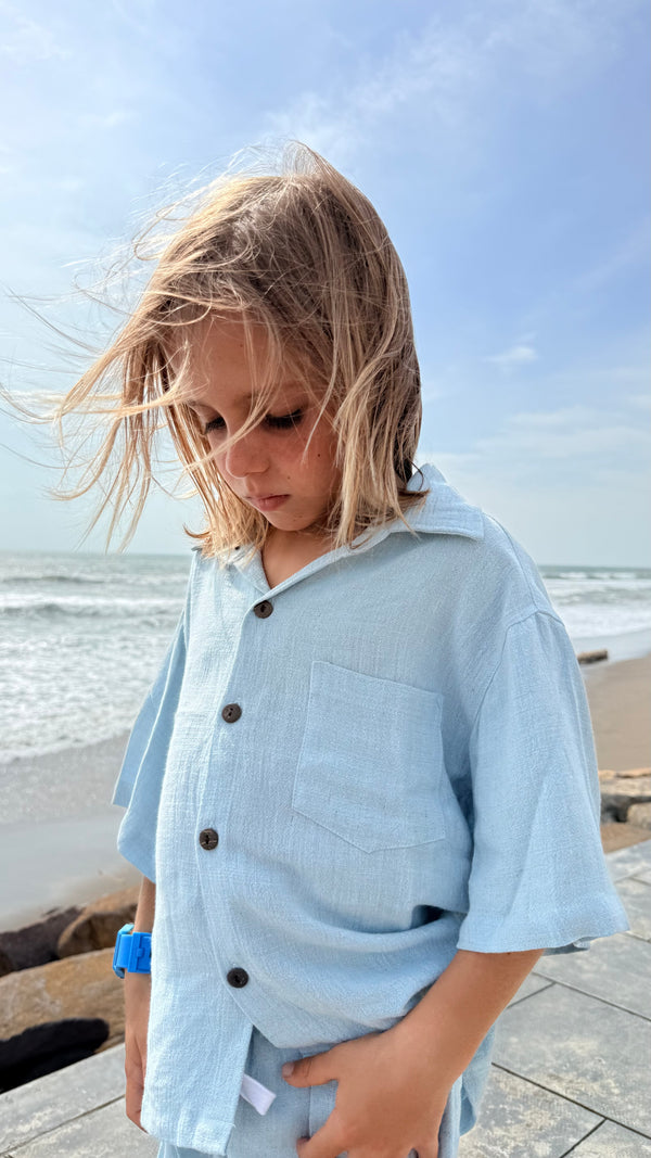 Child wearing a light blue shirt with buttons by the beach