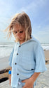 Child wearing a light blue shirt with buttons by the beach