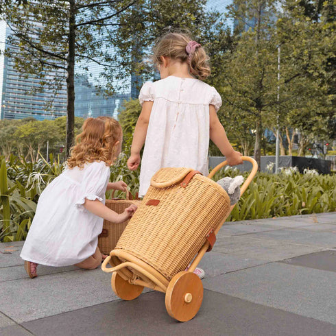 Two children playing with a wicker doll pram in an outdoor setting.