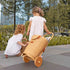Two children playing with a wicker doll pram in an outdoor setting.