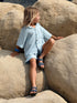 Child sitting on large rocks wearing a light blue shirt and dark sandals.