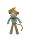 A crochet doll representing a red monkey with a blue shirt and a green accessory on its head, standing upright on a wooden surface.