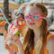 Children wearing colorful sunglasses eating watermelon outdoors.