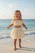 Child in a yellow outfit standing on a beach with ocean waves in the background