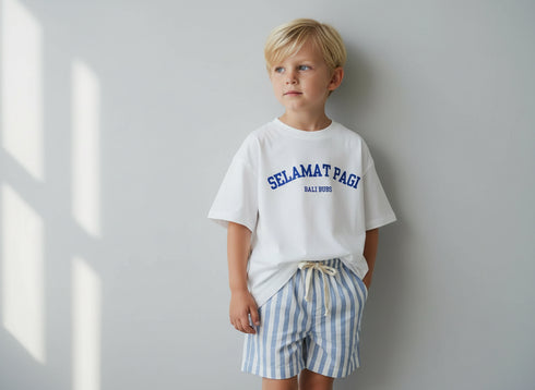 Child wearing a white t-shirt with 'Selamat Pagi' text and striped shorts against a light background