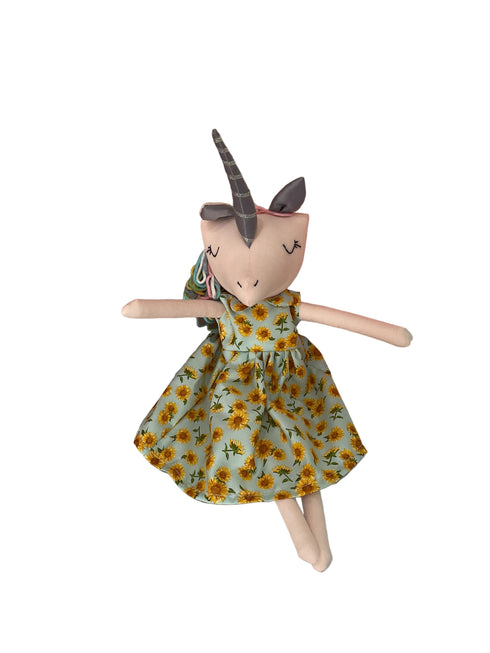 A plush unicorn doll with a gray horn and closed eyes, wearing a yellow sunflower dress.