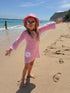 Child in a pink crochet dress and hat on a beach