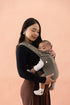 Woman holding a baby in a green baby carrier against a pink background