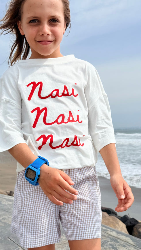 Child wearing a white shirt with 'Nasi Nasi Nasi' text by the ocean