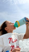 Person drinking from a colorful water bottle against a clear sky.