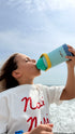 Person drinking from a colorful water bottle against a clear sky.
