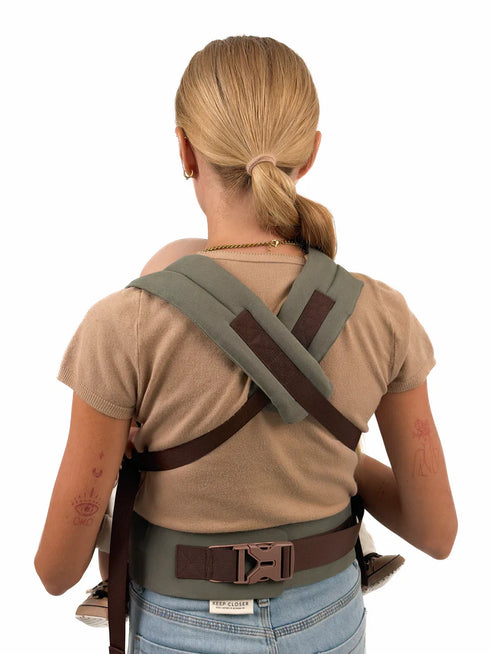 Person wearing a green and brown tactical belt with shoulder straps on a white background