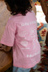 Child wearing a pink t-shirt with text and graphics, standing on a wooden floor.
