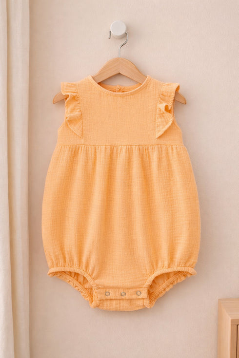 Yellow baby romper on a wooden hanger against a beige wall