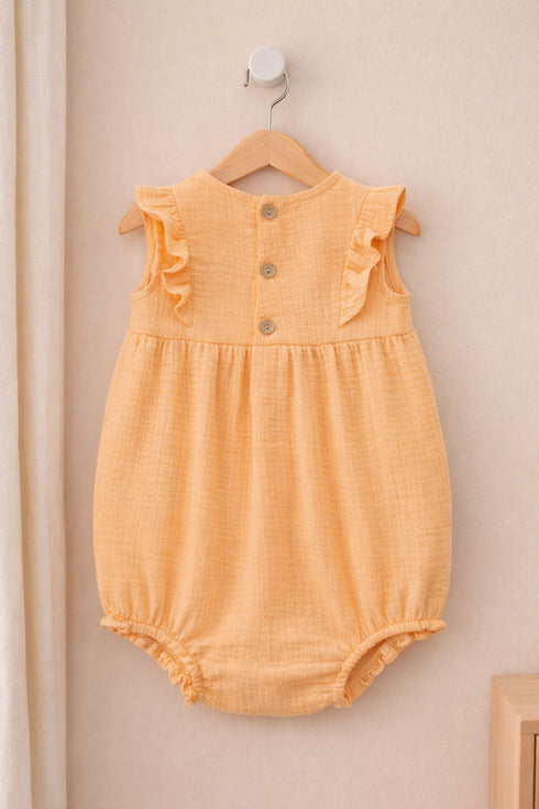 Yellow baby romper with ruffled details on a wooden hanger against a beige wall.