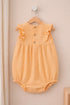 Yellow baby romper with ruffled details on a wooden hanger against a beige wall.