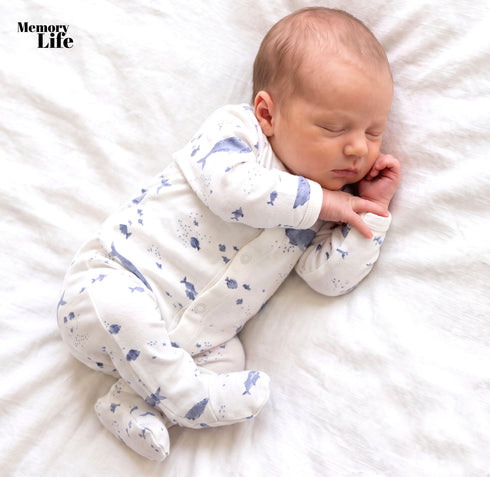 A sleeping newborn baby wearing a white footed sleeper with a blue fish pattern