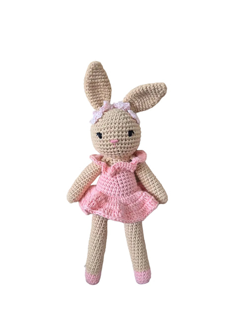 A crocheted stuffed bunny doll with long tan ears, a pink dress, and a small pink bow