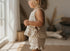 Child wearing a crochet outfit standing by a window in a softly lit room.