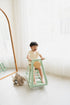 Child playing on a green toy in a room with white walls and a wooden floor.