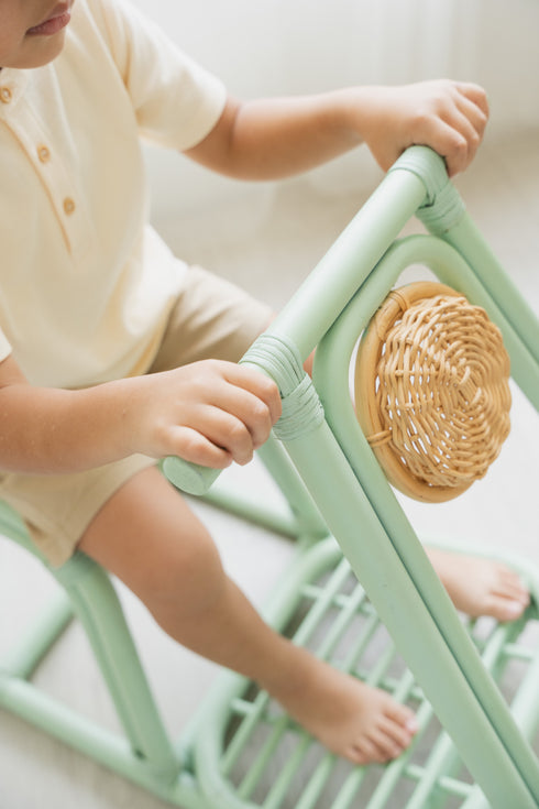 Child sitting on a light green chair with woven seat pad in a minimalistic setting