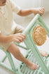 Child sitting on a light green chair with woven seat pad in a minimalistic setting