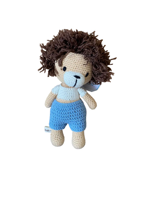 Crocheted toy lion with blue shorts on a wooden surface