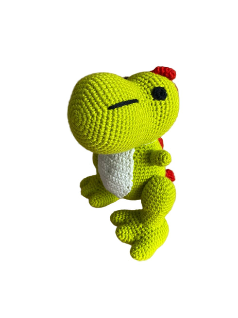 Crocheted green dinosaur toy on a reflective surface with blurred background