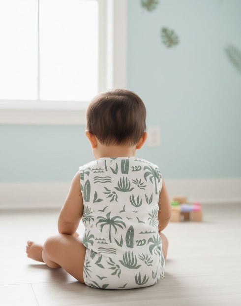 Child wearing a sleeveless shirt with green patterns sitting on the floor.