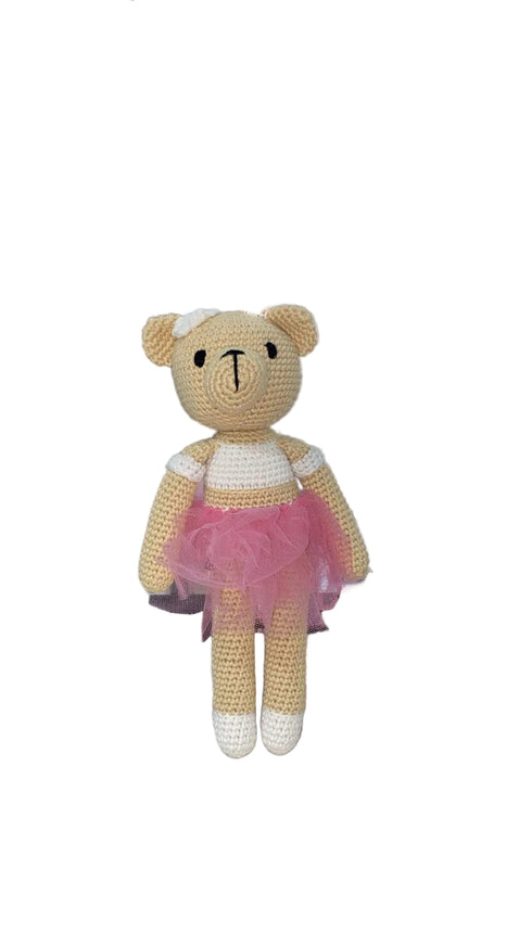 Crocheted teddy bear in a pink dress on a white surface
