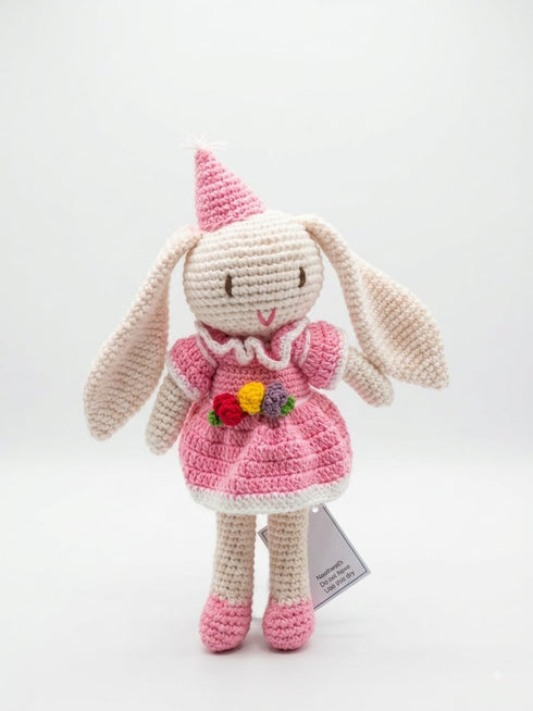 A handmade crocheted bunny doll wearing a pink dress, pink shoes, and a pink party hat