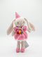 A handmade crocheted bunny doll wearing a pink dress, pink shoes, and a pink party hat