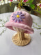 Pink crochet hat with a purple flower on a mannequin head against a light background.