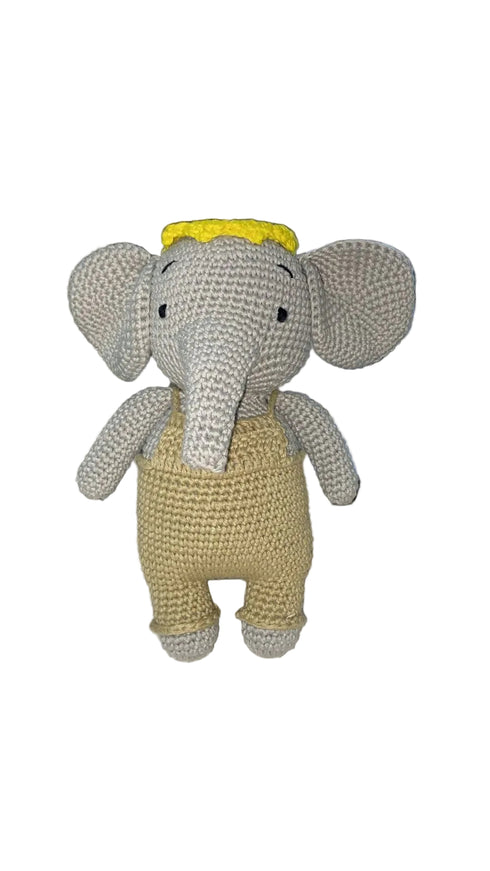 Crocheted elephant toy with a yellow hat on a white surface.