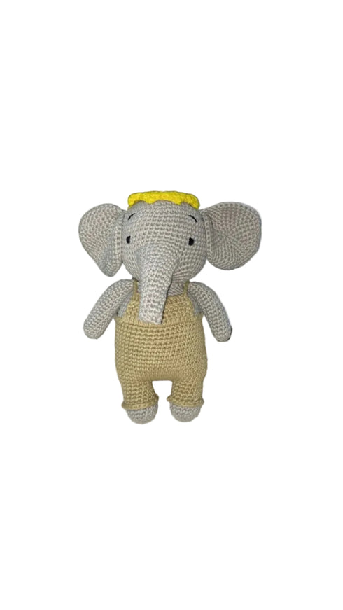 Crocheted elephant toy with a yellow hat on a white surface.