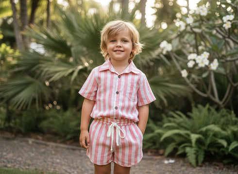 Child wearing a pink and white striped outfit standing in a garden.