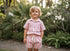 Child wearing a pink and white striped outfit standing in a garden.