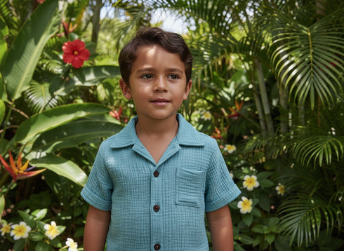 Child in a blue shirt standing in a lush garden with flowers and greenery