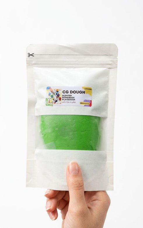Hand holding a package of green play dough with a visible brand label on a white background