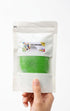 Hand holding a package of green play dough with a visible brand label on a white background
