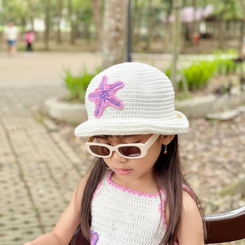 Child wearing a white hat with a starfish design and sunglasses in a park setting