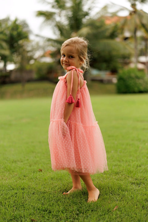 pink tiered tulle dress with tie-shoulder straps and pink tassel accents.