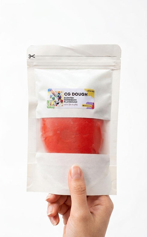 Hand holding a package of red play dough with a visible brand label on a white background