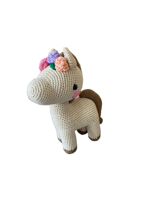 Crocheted unicorn toy with floral crown on a blue surface with wooden panel background